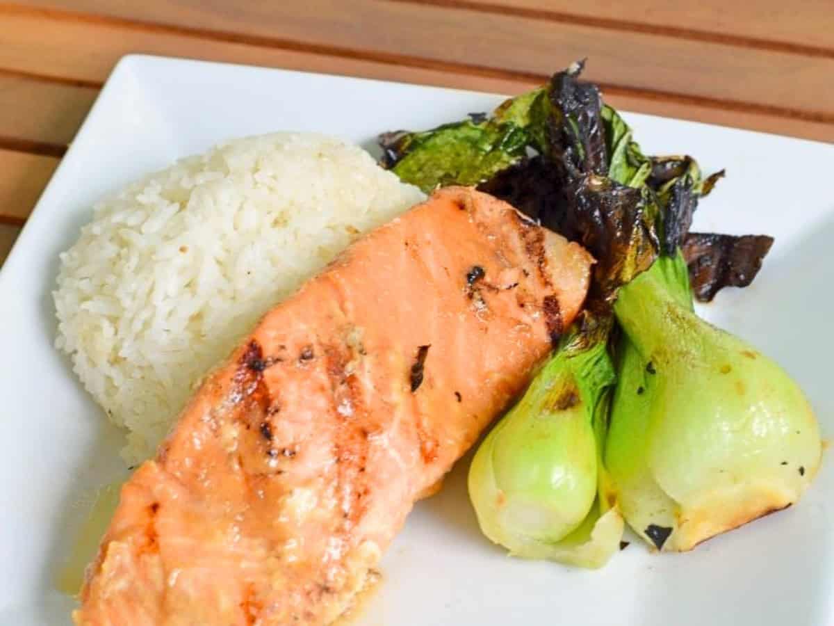 Sous vide miso glazed salmon served with white rice and charred baby bok choy on a square white plate.