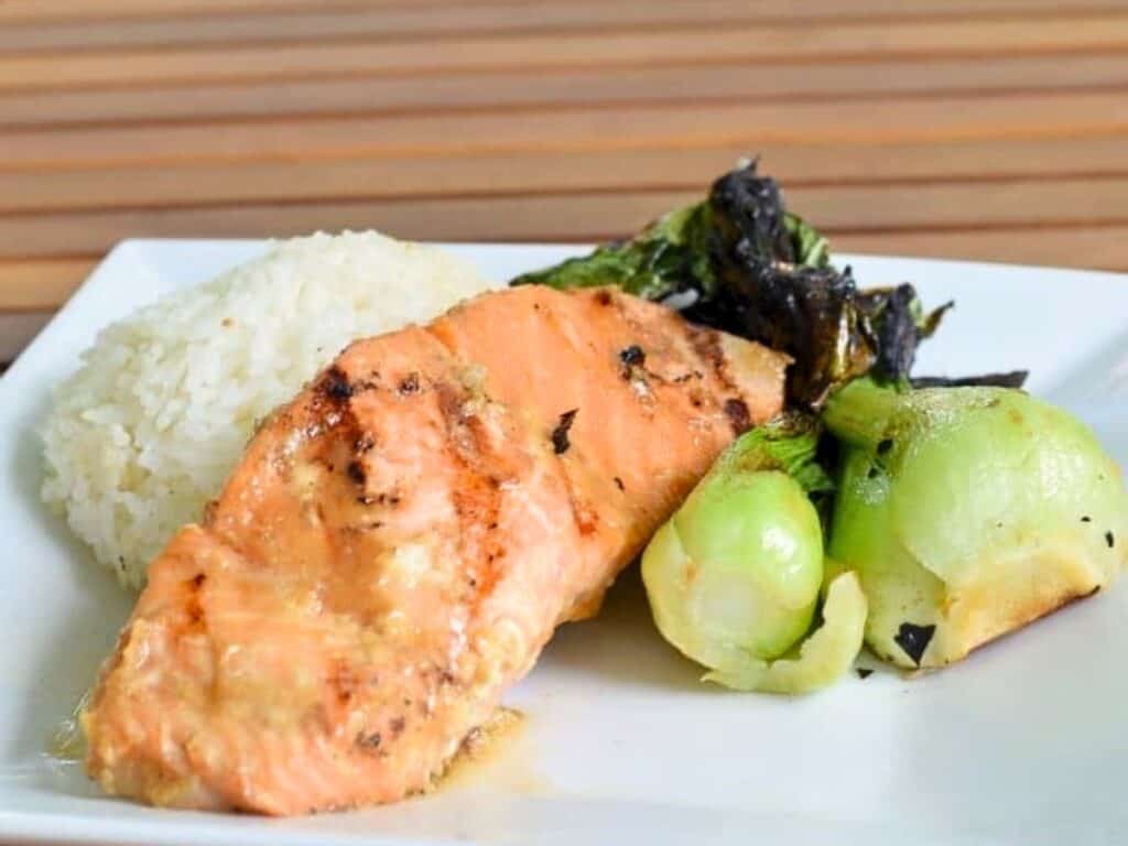 Sous vide miso glazed salmon fillet served with white rice and sautéed bok choy on a white square plate.