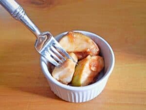 A fork rests on a white ramekin filled with Instant Pot cinnamon apples—sliced apples coated in warm cinnamon and sauce—placed on a wooden surface.