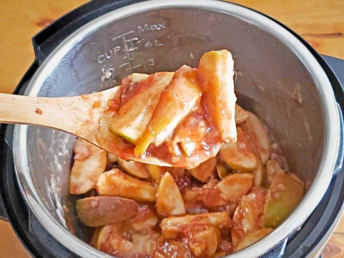 Sliced apples in a thick sauce being stirred with a wooden spoon inside a metal pot, likely for cooking or baking delicious Instant Pot cinnamon apples.