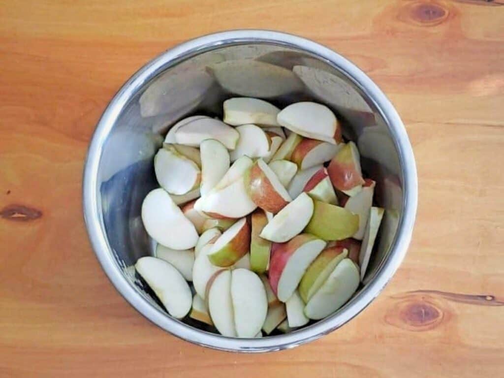 A metal bowl filled with sliced apples, reminiscent of Instant Pot cinnamon apples, sits on a wooden surface.