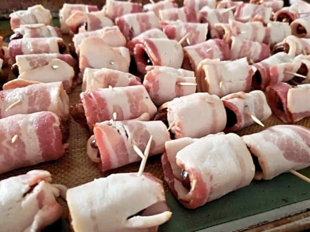 Rows of bacon wrapped dates, each secured with a toothpick, are arranged on a baking tray, ready to be cooked.