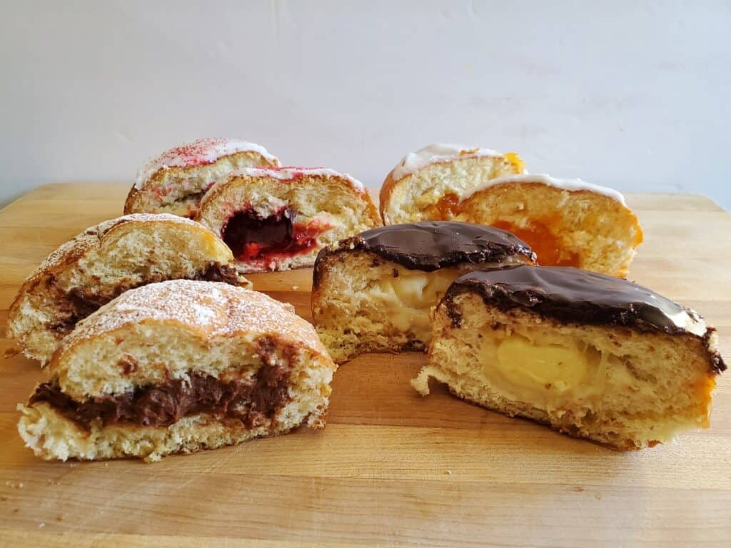 Four paczki flavors from Bennisons bakery cut in half sitting on a wooden board.