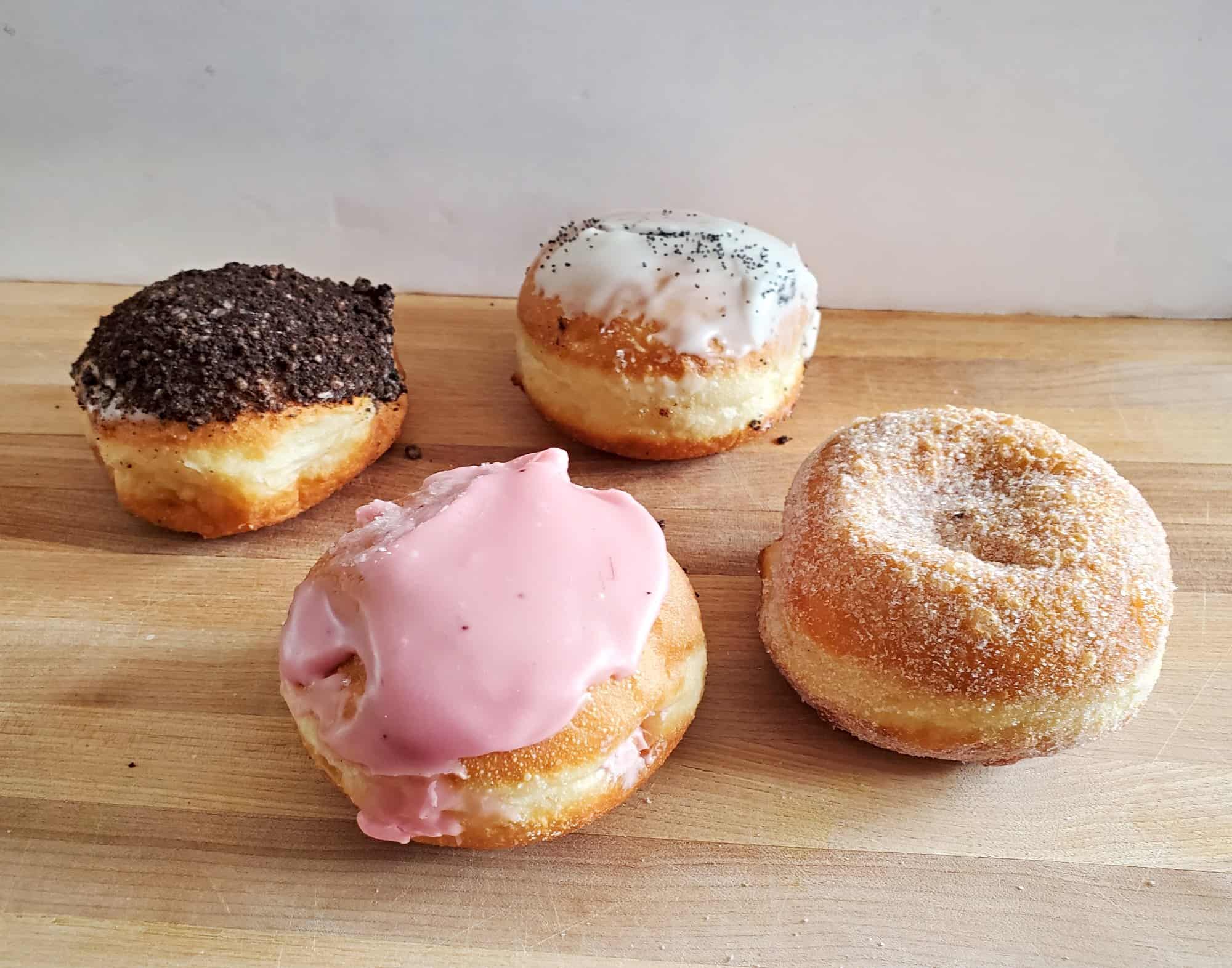 Four paczki from Weber Bakery in Chicago are sitting on a wooden cutting board.