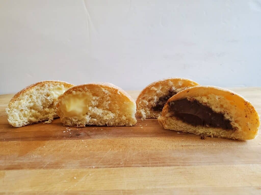 Hewn Bread Lemon and chocolate paczki cut in half sitting on a wooden board.