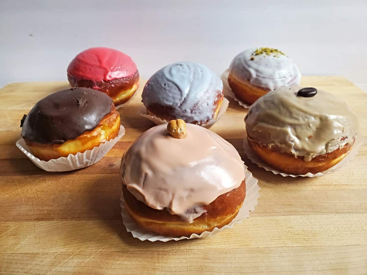 Six different fancy paczki on a wooden board.