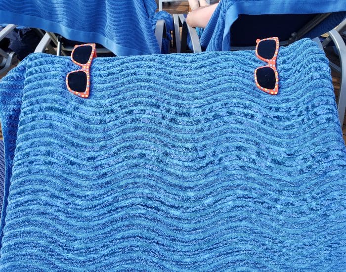 Two sunglasses shaped towel clips attached to a blue beach towel on a lounge chair.