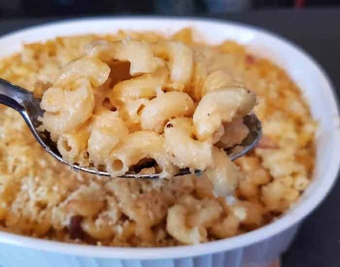 Image shows a Scoop of bacon mac and cheese with the entire casserole behind it.