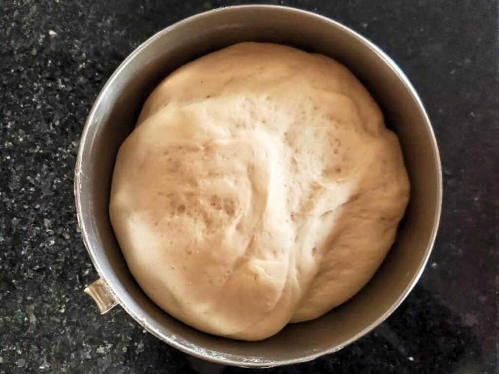 A bowl filled with risen bread dough, soon to be shaped into delicious pretzel bites, sits on a dark countertop.