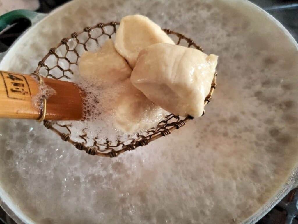 Chunks of dough, soon to become delicious pretzel bites, are being lifted from boiling water with a wire skimmer.