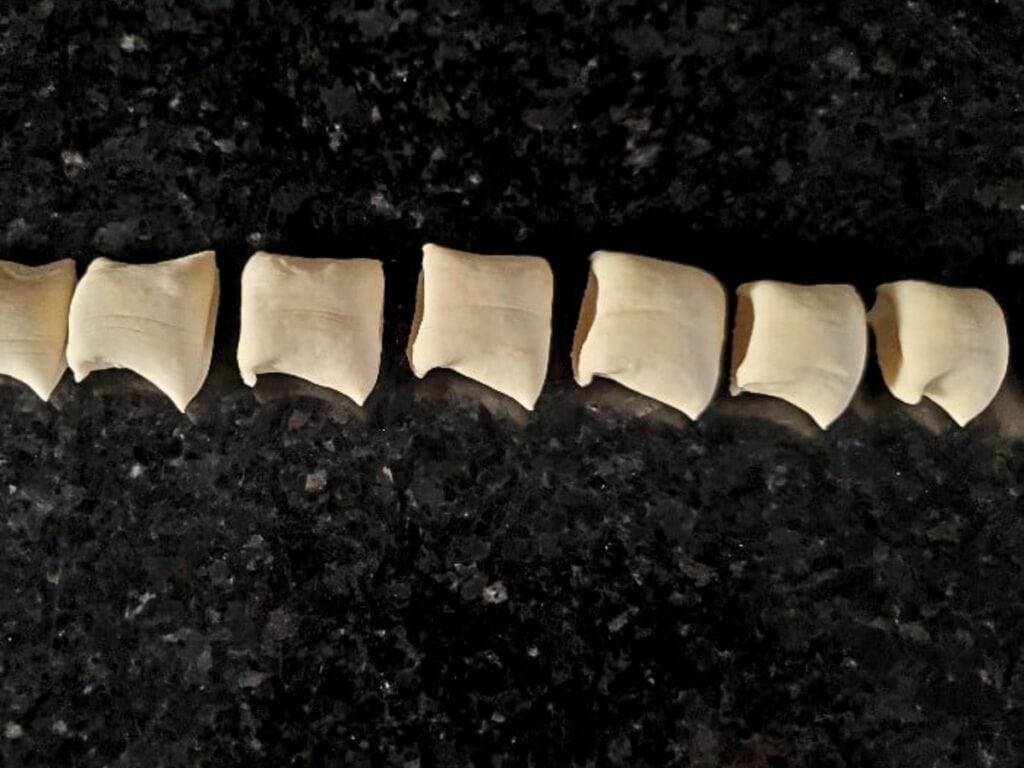 Eight pieces of uncooked pretzel bites dough are lined up in a row on a dark, speckled countertop.