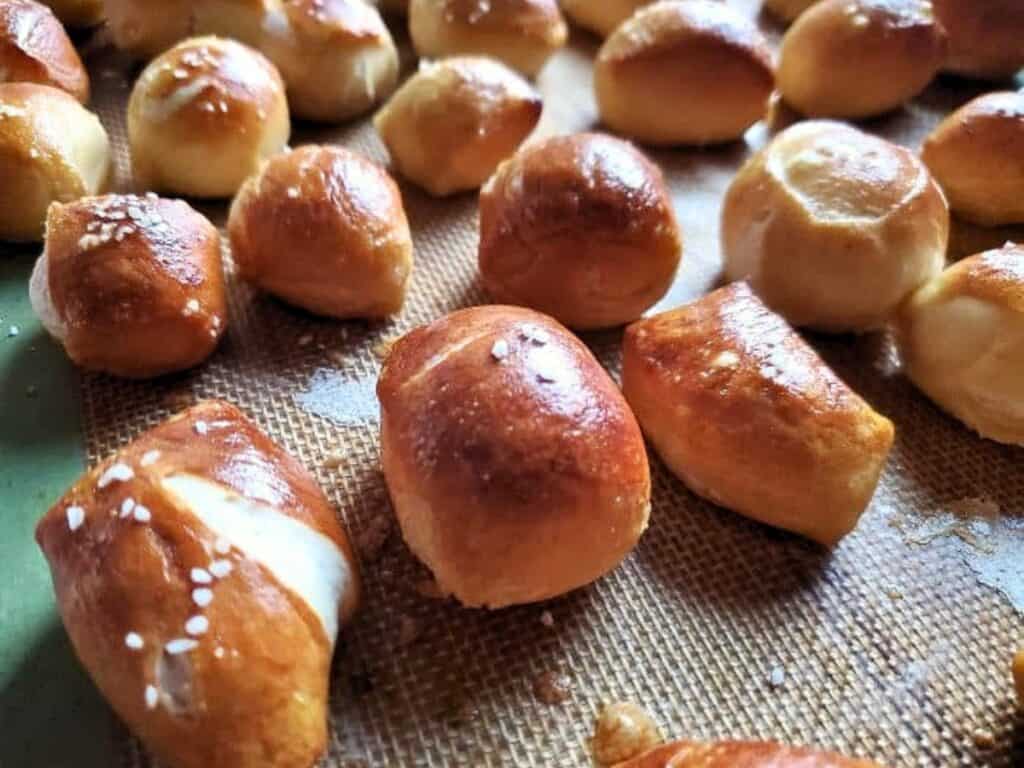 Small golden-brown pretzel bites rest on a baking mat, some topped with salt, arranged in close rows for the perfect bite-sized snack.