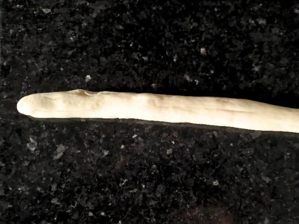 A long, thin strip of raw dough, soon to be transformed into delicious pretzel bites, is placed on a dark, speckled countertop.
