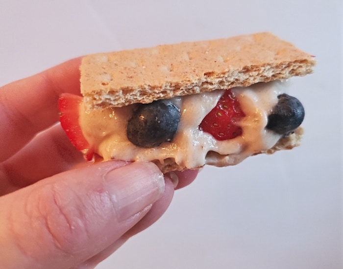 Image shows Banana ice cream sandwiches with strawberries and blueberries on a wooden board.