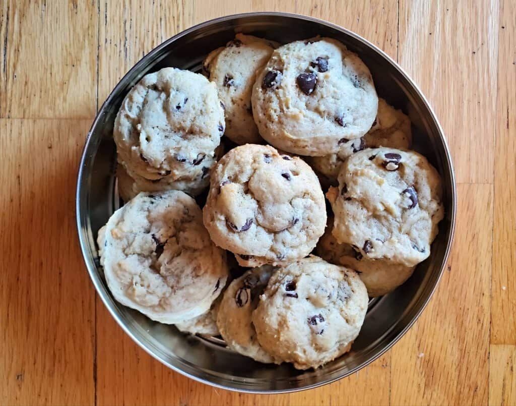 Image shows a Tin of chocolate chip cookies on a wooden background.