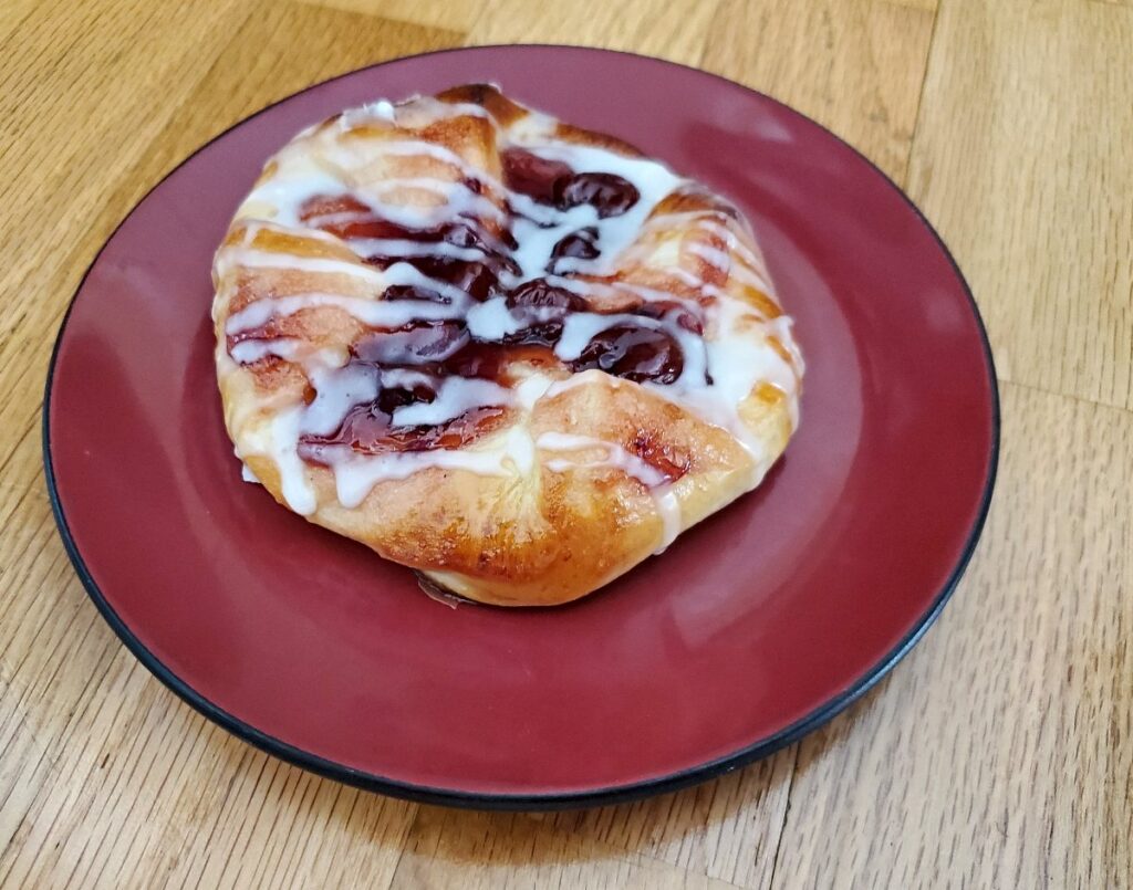 Red plate with a homemade cherry danish on it.