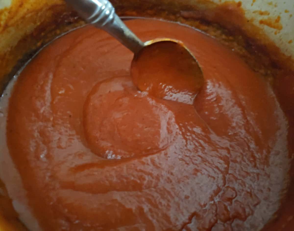 Stirring homemade enchilada sauce in a pot with a silver spoon.