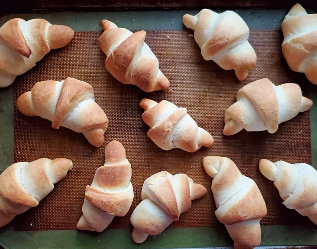 Baking pan with homemade crescent rolls scattered on it.