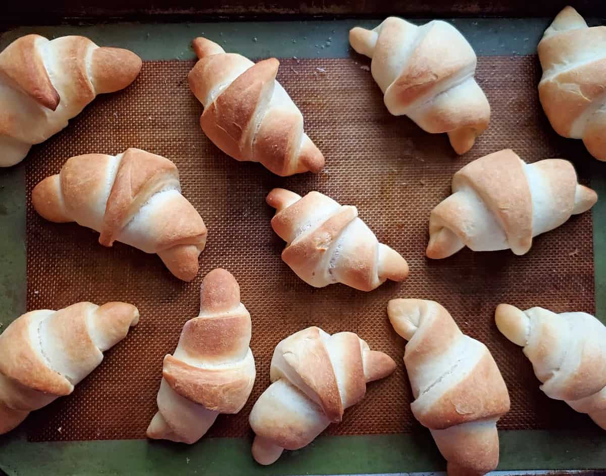 Baking pan with homemade crescent rolls scattered on it.