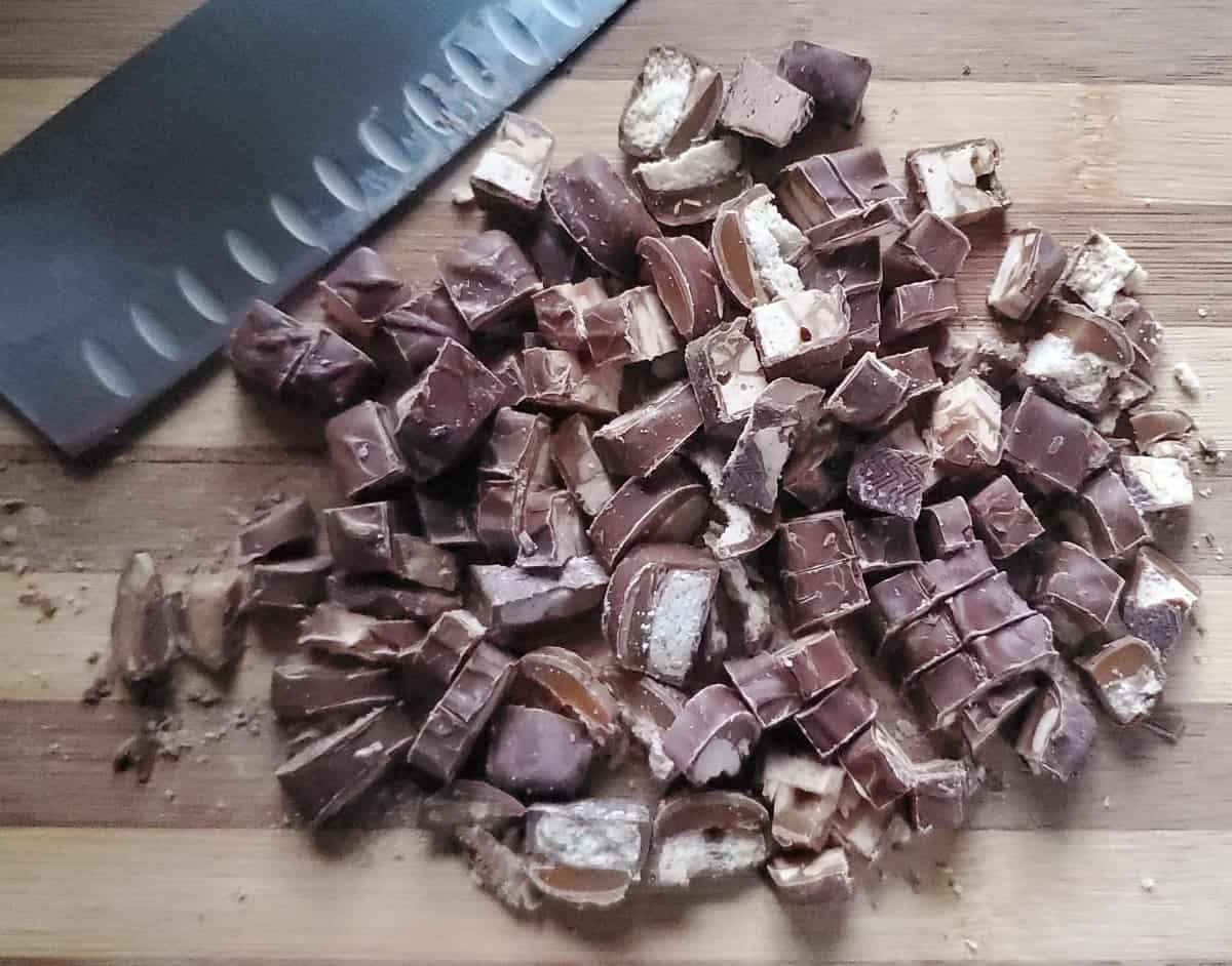 Chopped candy bars on a wooden cutting board with a knife.