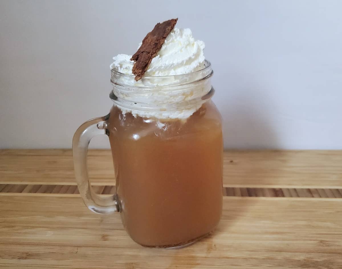 Mug of spiked apple cider topped with whipped cream and a cinnamon stick.