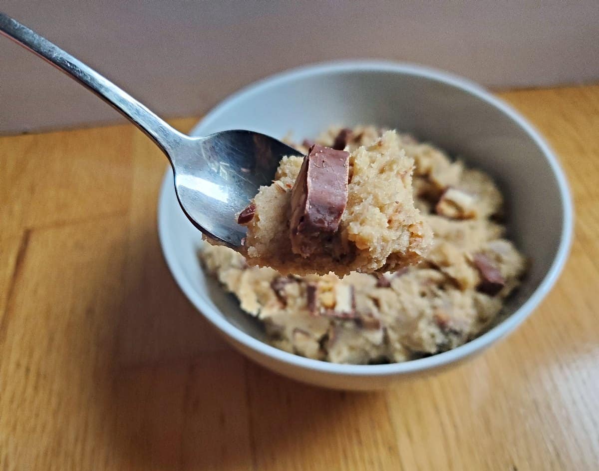 Spoon of edible cookie dough over a bowl of more.