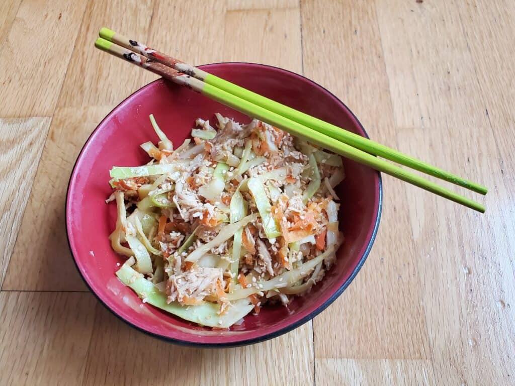 Overhead of a red bowl of egg roll in a bowl with chopsticks resting on the bowl.