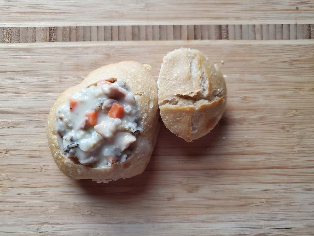 Overhead of wild rice soup in a bread bowl on a wooden board.