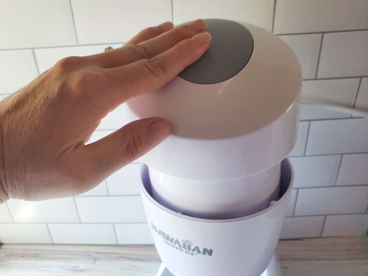 Hand pressing the power button on a shaved ice machine.