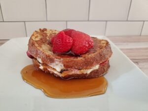 Strawberry stuffed french toast with syrup on a white plate.
