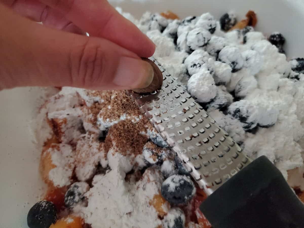 Grating nutmeg onto cornstarch covered fruit.