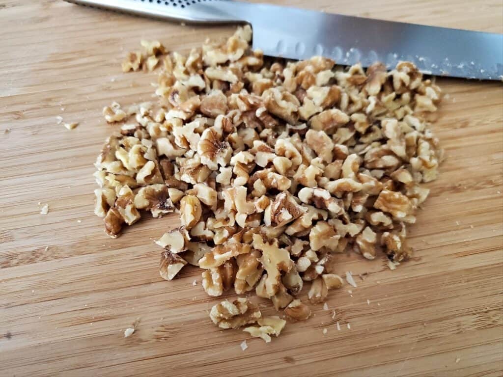 Chopped walnuts with a knife on a cutting board.