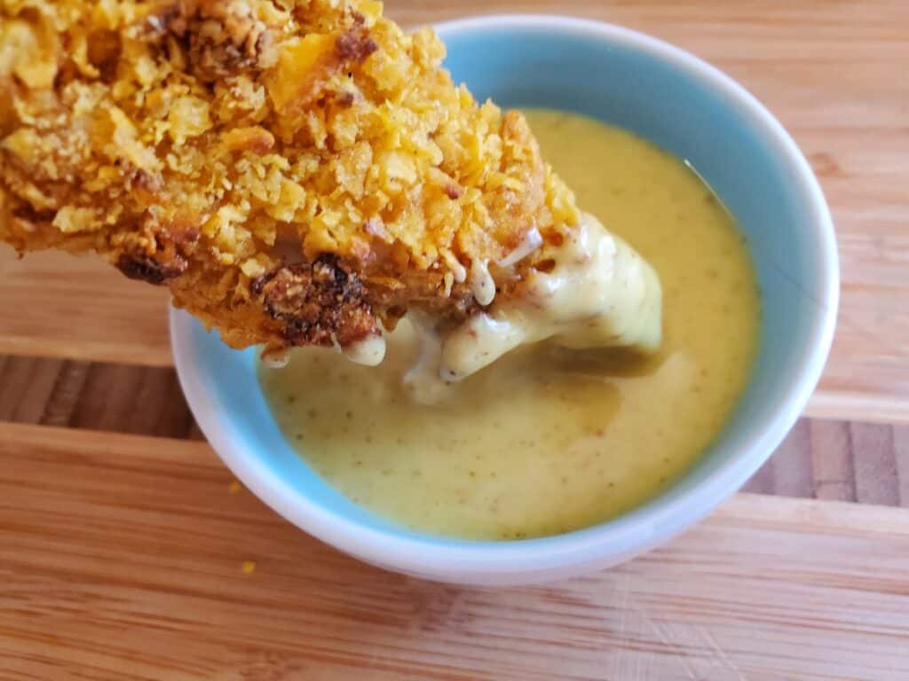 Close up of a gluten free chicken tender dipping into honey mustard.
