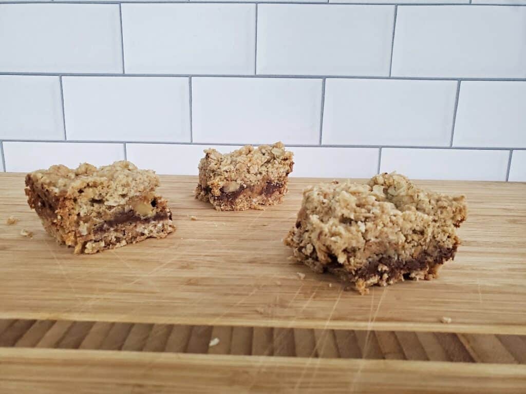 Three chocolate caramel bars sitting on a wooden board.