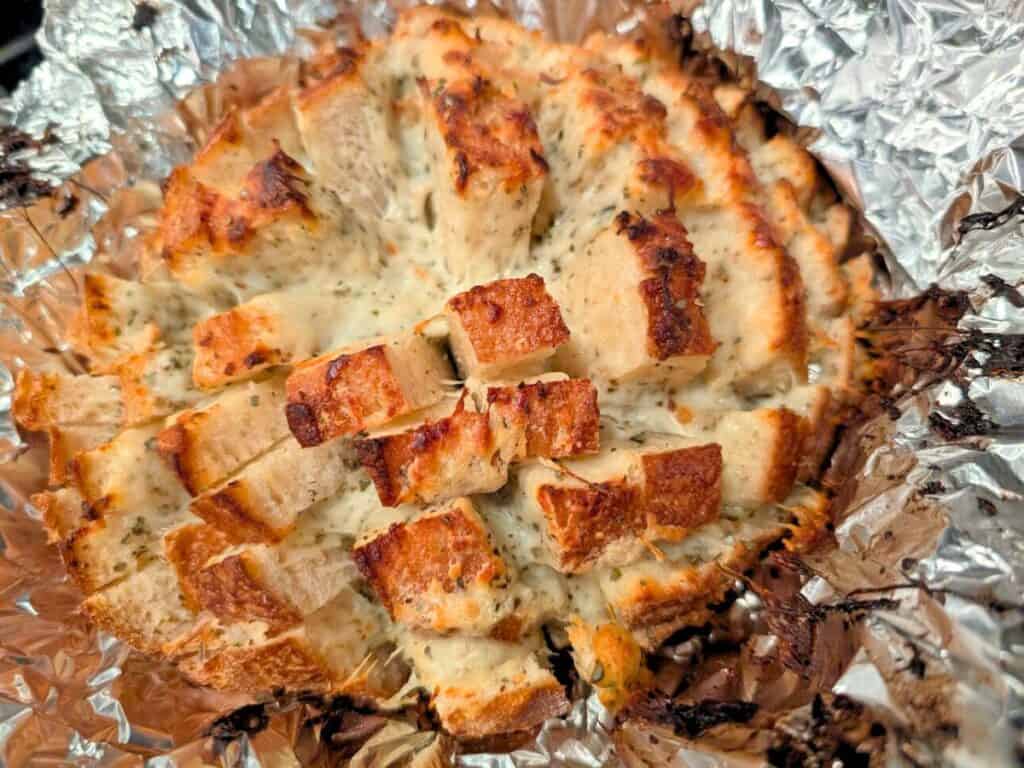 Image shows baked pull-apart bread with melted cheese in foil.