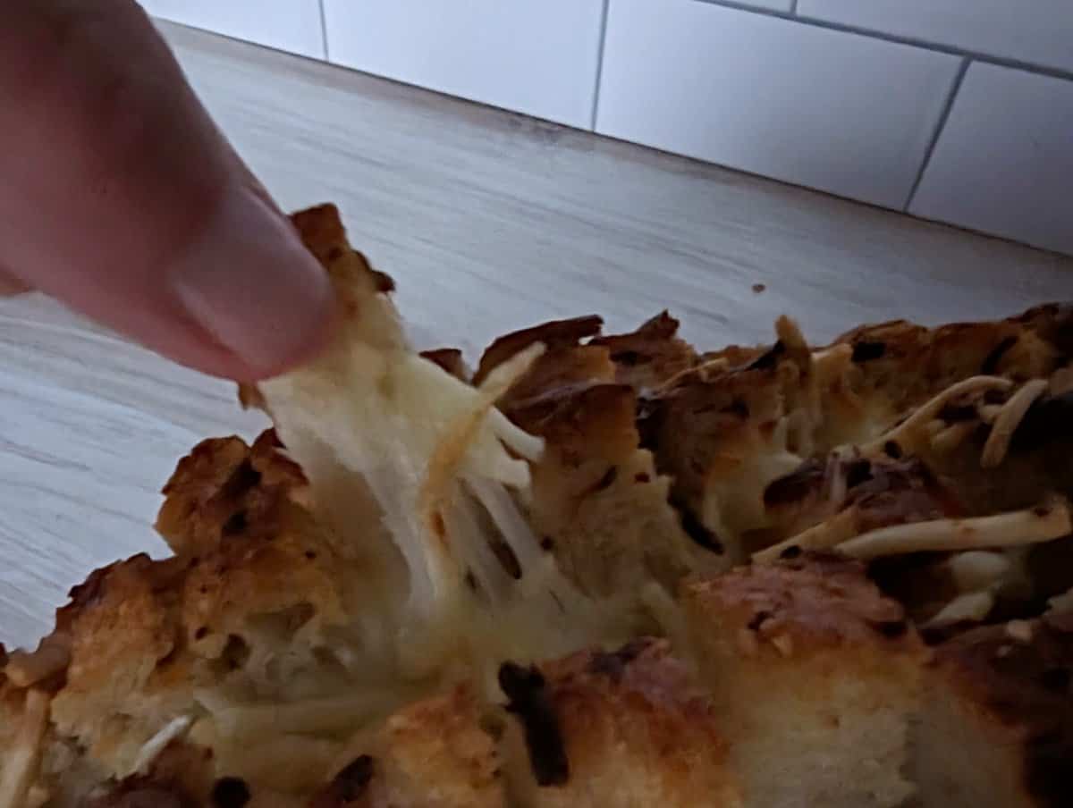 Hand pulling off a piece of cheesy garlic pull apart bread.