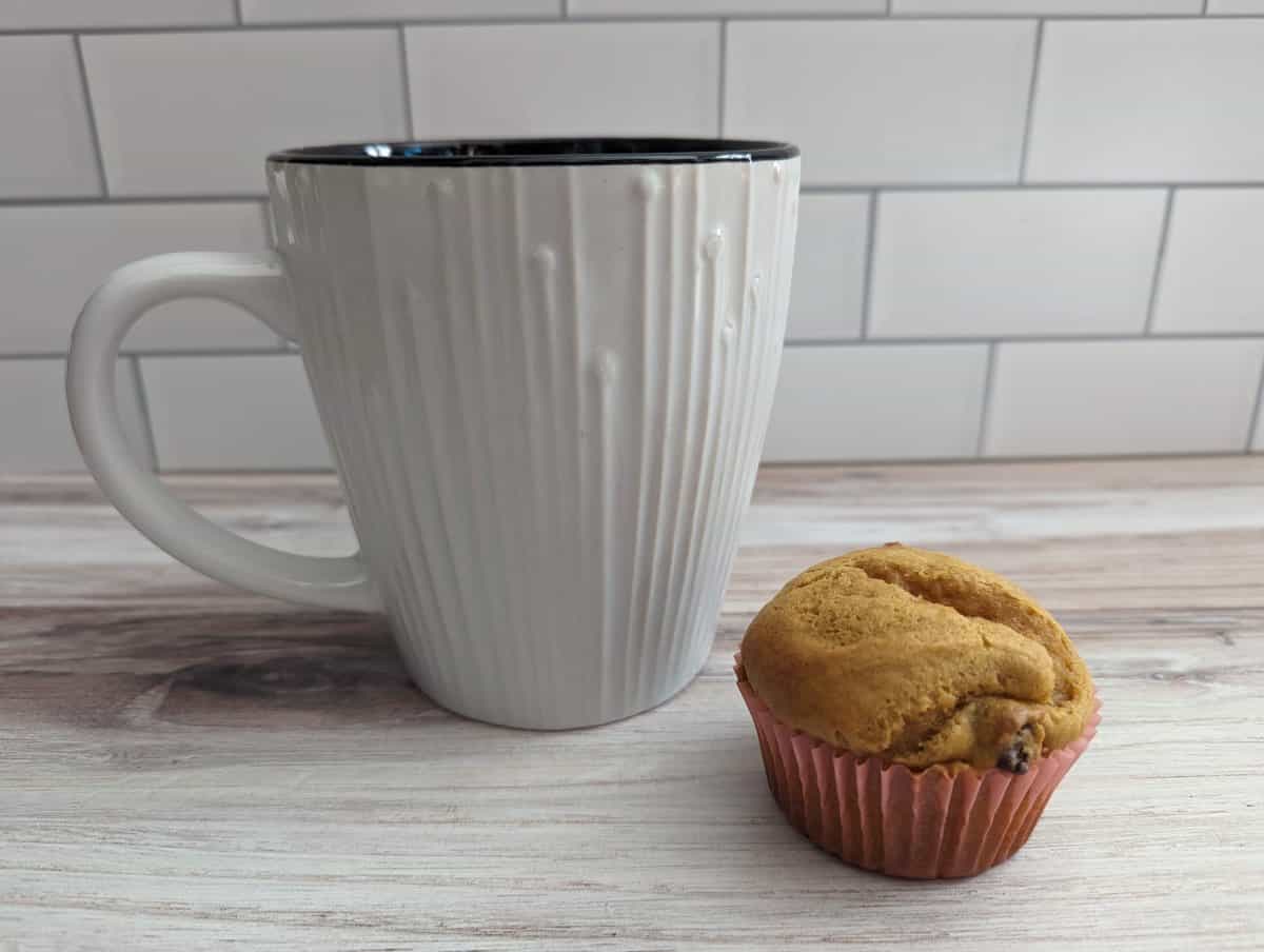 Mug of coffee with a pumpkin muffin next to it.
