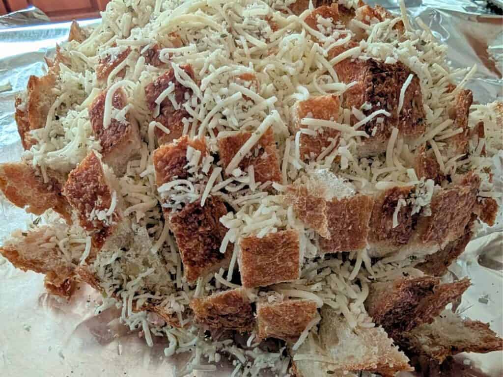 Image shows sourdough bread covered with shredded cheese, ready to bake on foil.