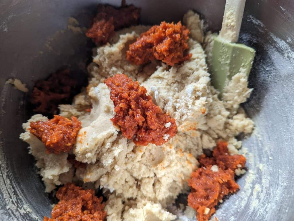 Bowl with cookie dough and dollops of gochujang caramel sauce and spatula in the back of the bowl.