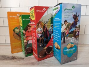 Four different Girl Scout Cookie flavor boxes standing on a wood background.