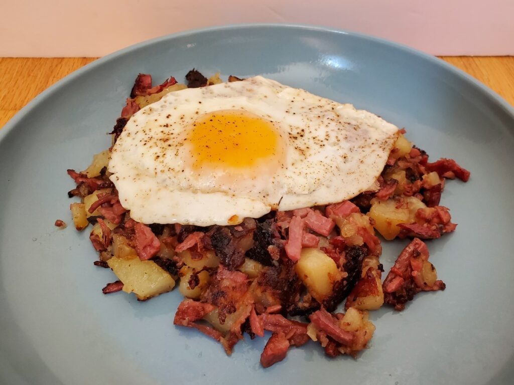 Fried egg over corned beef hash on a blue plate.