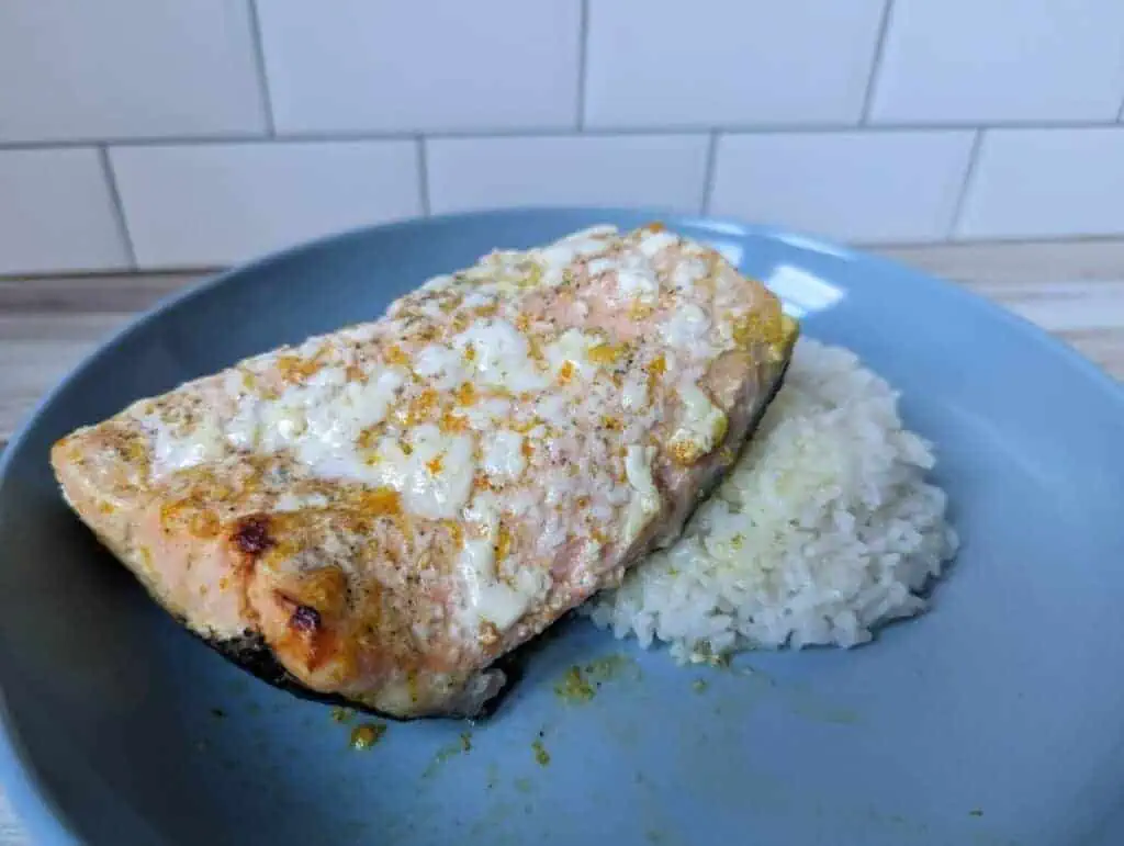 Orange salmon on a blue plate with rice with albumin on top of the salmon.