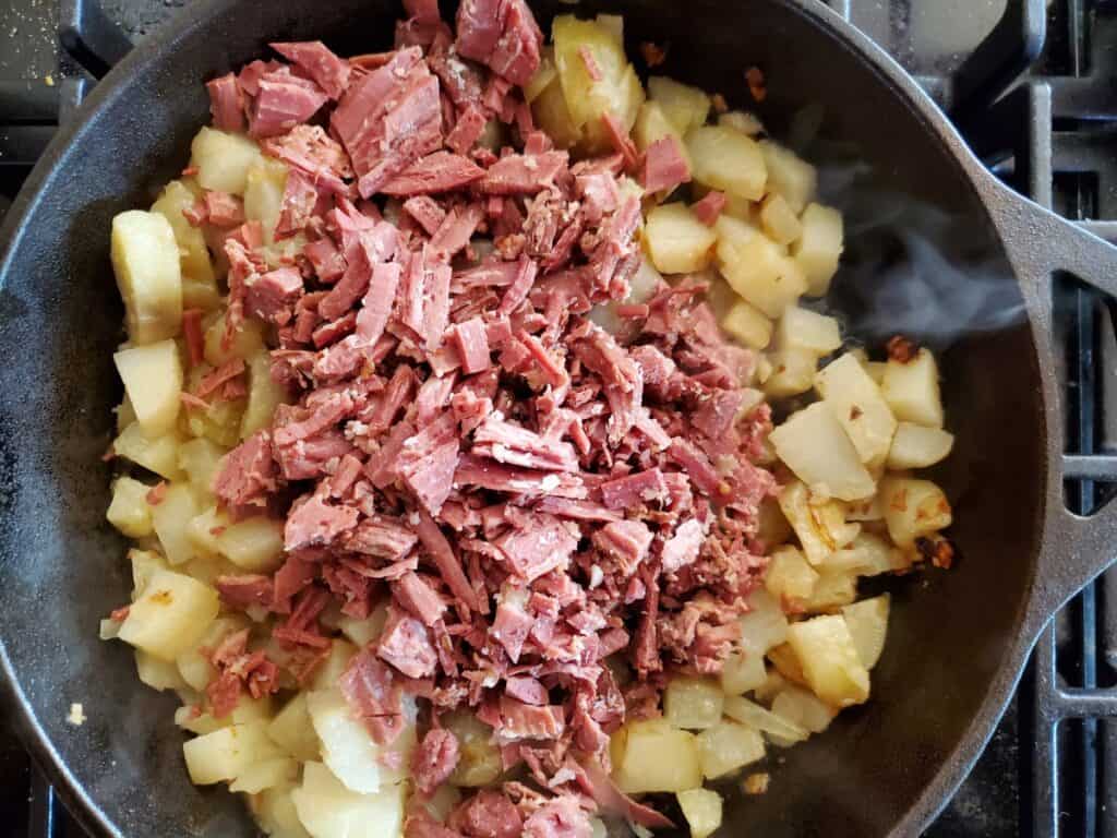 Overhead shot of potatoes and corned beef in a cast iron skillet.