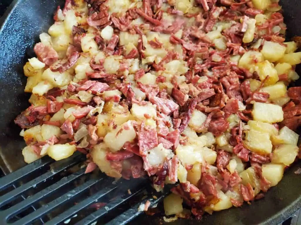 Spatula about to flip corned beef hash in a cast iron skillet.