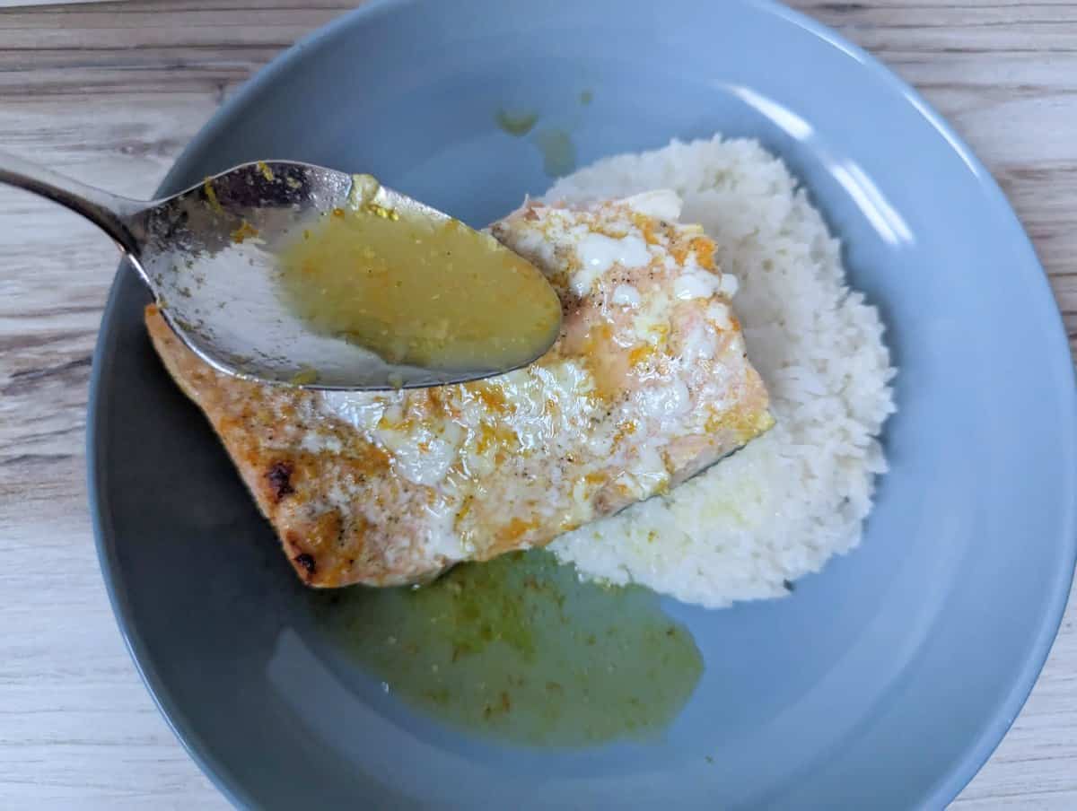 Image shows a spoon drizzing orange sauce over a salmon filet in a blue dish.