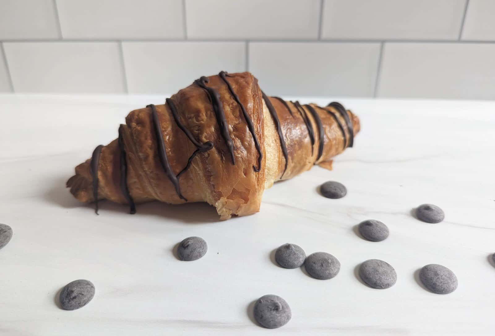 Chocolate drizzled croissant on a white background with chips around it.