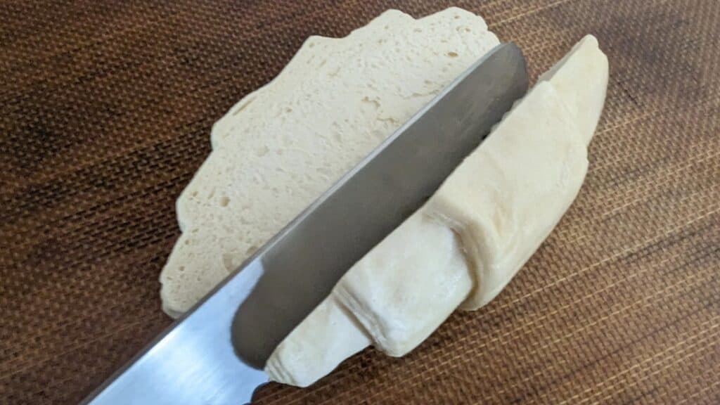 Knife cutting a raw croissant in half.
