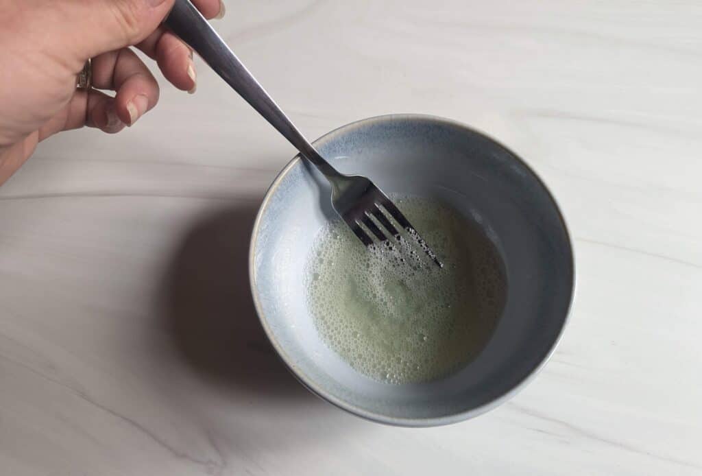 Overhead of a hand stirring egg wash in a bowl.