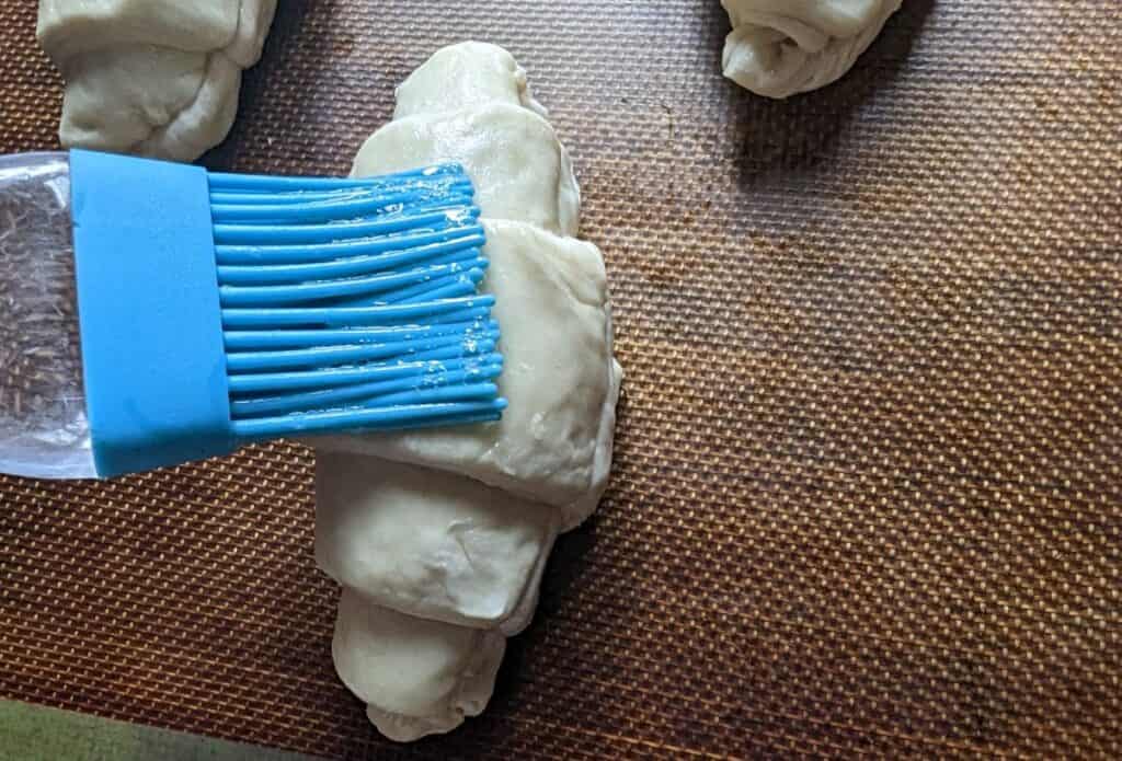 Pastry brush adding egg wash to formed croissants.