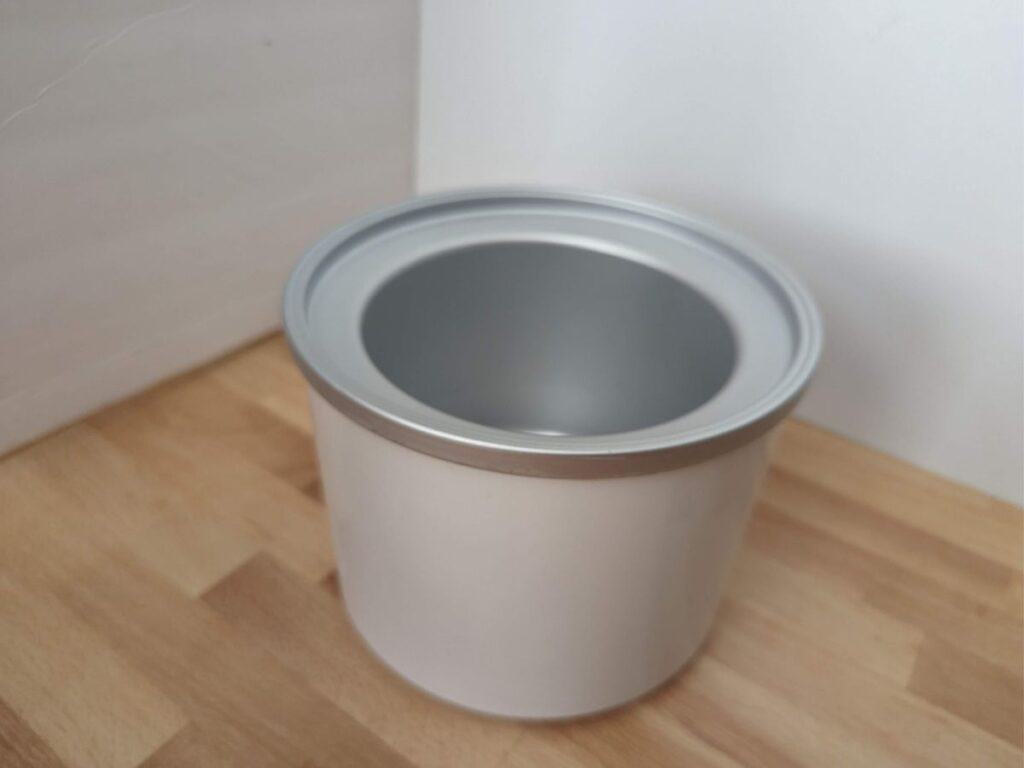 Image shows an extra freezer bowl for an ice cream maker sitting on a wooden table.
